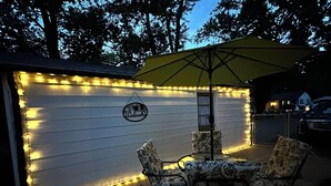 A patio area with a table and chairs, a yellow umbrella, and string lights on a wall. - Cozy Cottage - Pet-Friendly with Fenced Yard (Evansville)