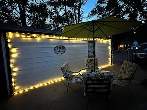 A patio area with a table and chairs, a yellow umbrella, and string lights on a wall.