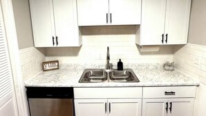 A kitchen with white cabinets, a double sink, a dishwasher, and a 'home' doormat. - Cozy Cottage - Pet-Friendly with Fenced Yard (Evansville)