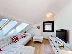 A modern loft bedroom with a white sofa, a small white ottoman, a flat-screen TV, and a skylight. - Charming Duplex for 4 in the Heart of Morzine (MORZINE)