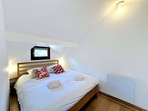 A bedroom with a bed, pillows, a nightstand, a wall-mounted light, and a window. - Charming Duplex for 4 in the Heart of Morzine (MORZINE)