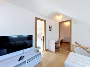 A modern living room with a flat-screen TV, a white sofa, a dining table with chairs, and a small white cabinet. - Charming Duplex for 4 in the Heart of Morzine (MORZINE)