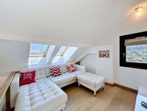 A modern living room with a white sectional sofa, a small ottoman, and a wall-mounted sign that reads 'EAT SLEEP SKI'. - Charming Duplex for 4 in the Heart of Morzine (MORZINE)