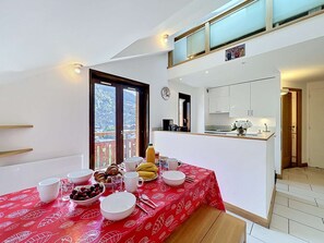 Ein Essbereich mit einem für das Frühstück gedeckten Tisch, eine Küche mit weißen Schränken und ein Balkon mit Blick.