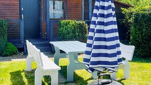 Un pati amb taula i bancs blancs, un para-sol estriat i una barbacoa.