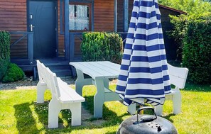 Eine Terrasse mit weißem Tisch und Bänken, einem gestreiften Sonnenschirm und einem Grill.