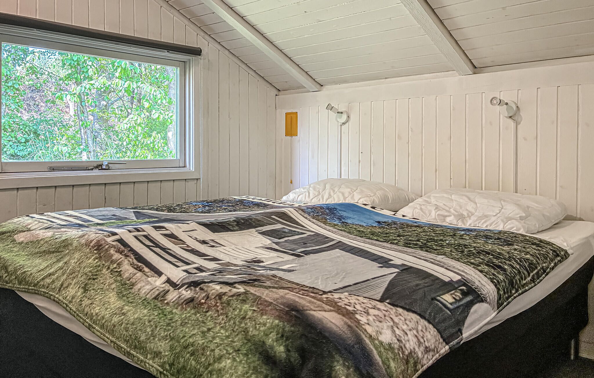 Une chambre avec une grande fenêtre, un lit recouvert d’une courtepointe à motifs et des murs recouverts de panneaux en bois.