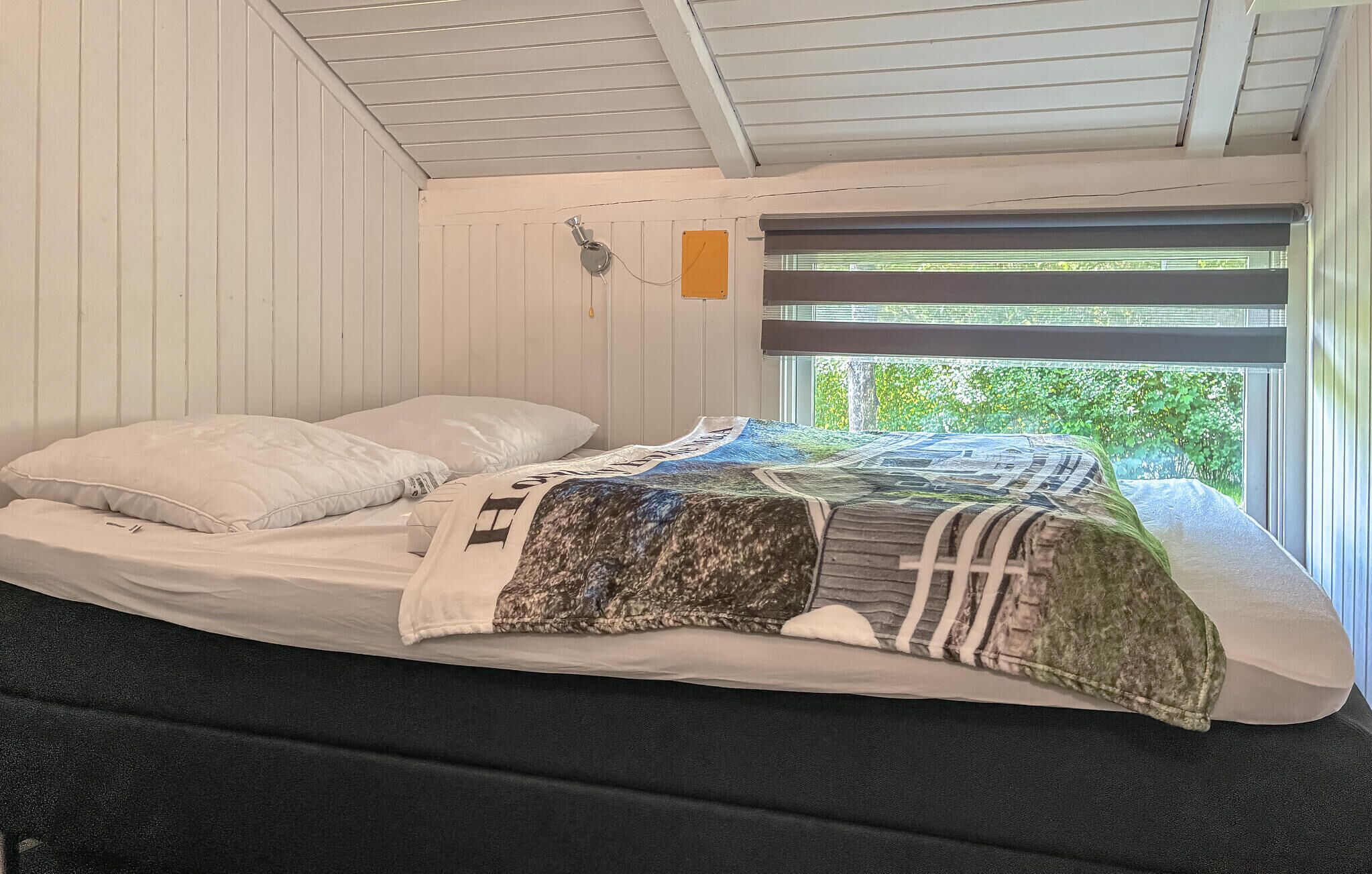 A single bed with a quilt, white walls, a window with blinds, and a ceiling fan.