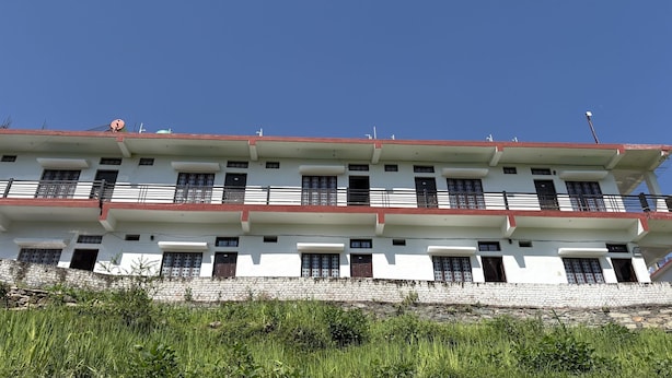 Um edifício com vários andares, varandas, um muro de pedra e um céu azul e límpido.