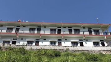 A multi-story building with balconies, a stone wall in front, and a clear blue sky.