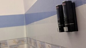 Uma casa de banho com sanita, lavatório e dispensador de sabonete fixado na parede.