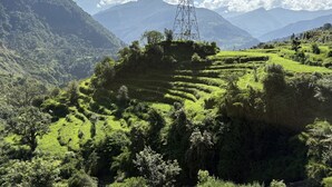 Paisagem montanhosa com campos em socalcos e uma torre de linhas de energia.
