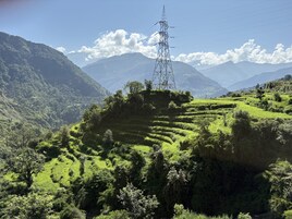 A mountainous landscape with terraced fields and a power line tower.