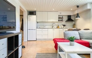 A modern kitchen with white cabinets, a microwave, and a dishwasher. There is a dining area with a white table and a red sofa.