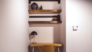 Quarto nos fundos com uma escrivaninha de madeira, uma cadeira, uma luminária e prateleiras com objetos decorativos.