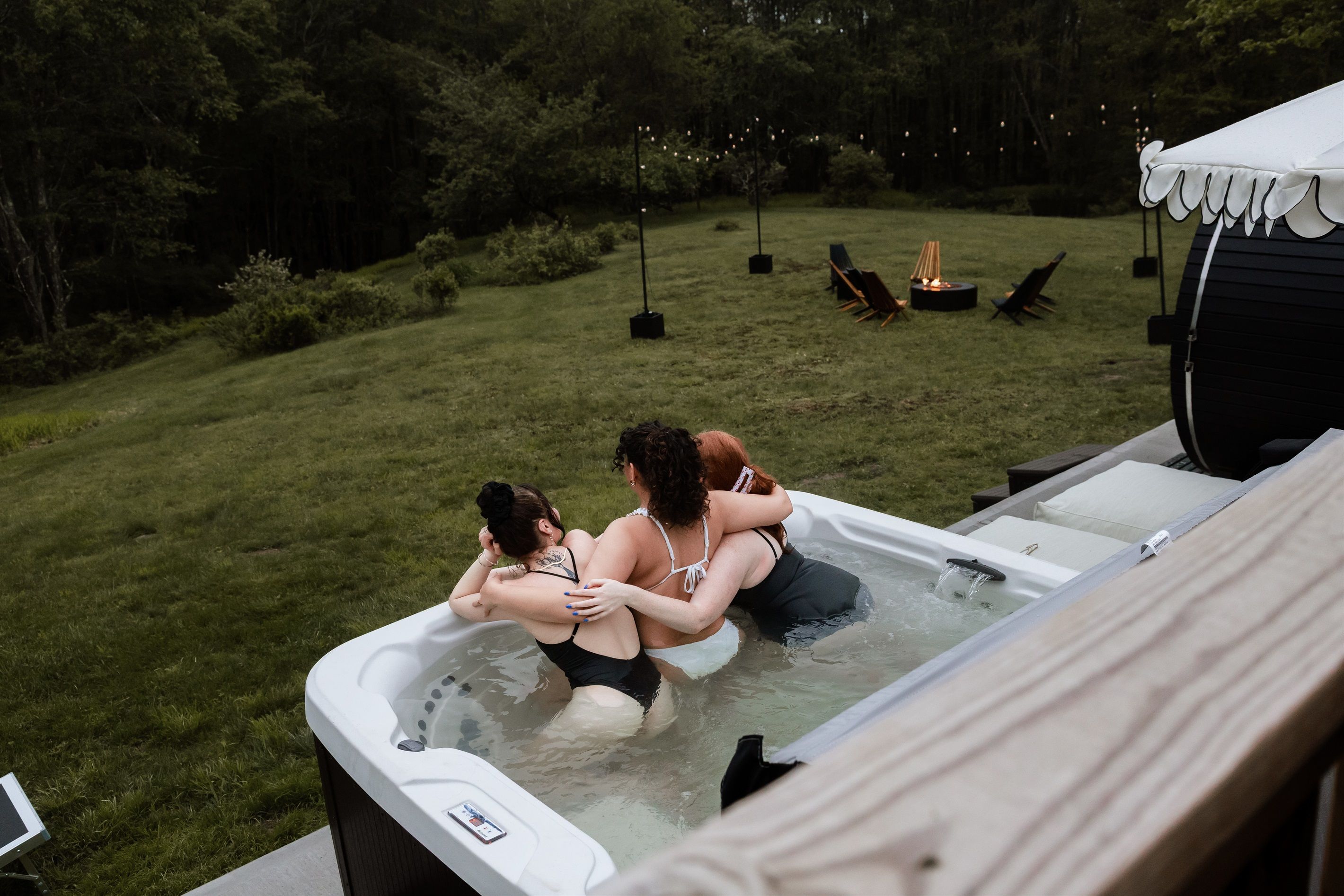 A hot tub with three people in it, surrounded by a grassy yard and outdoor furniture.