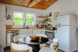 Une cuisine moderne avec des meubles blancs, une table ronde noire avec des chaises, un réfrigérateur et une fenêtre donnant sur un paysage verdoyant.