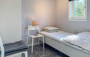 Ein kleines Zimmer mit einem Einzelbett, einem Nachttisch, einer Lampe, einem Stuhl und einem Fenster.