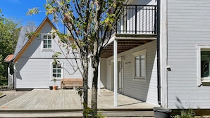Een wit gebouw met een houten terras, een kleine boom en een bankje.