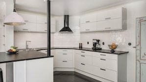 Een moderne keuken met witte kastjes, een zwart aanrecht, een roestvrijstalen afzuigkap en een hangende pendelarmatuur.