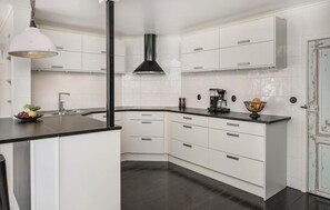 Eine moderne Küche mit weißen Schränken, einer schwarzen Arbeitsplatte, einer Edelstahl-Dunstabzugshaube und einer hängenden Pendelleuchte.