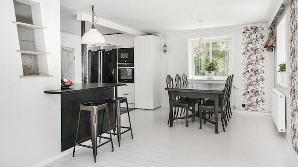 Een moderne keuken met een centraal eiland, barstoelen, een eettafel met stoelen, een groot raam en een radiator.