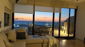 A living room with a sofa, a table, and a view of the ocean at sunset.