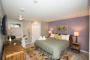 A bedroom with a bed, bedside tables, a desk, a television, and a painting on the wall.