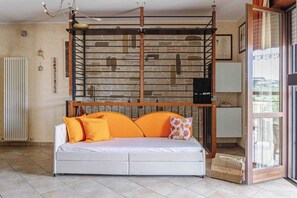 Ein Zimmer mit einer weißen Couch, einer Steinwand, einer Heizung und einem Fenster mit Jalousien.