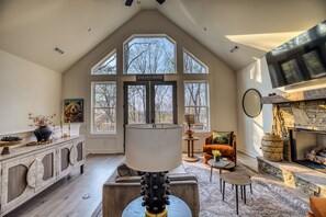 Ein geräumiges Wohnzimmer mit Kamin, großen Fenstern und hoher Decke.