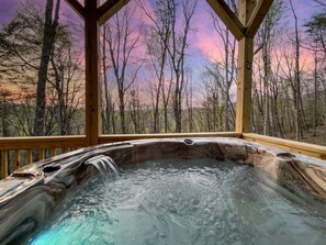 Een hottub met een houten terras, omringd door bomen en uitzicht op de lucht.