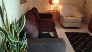 A living room with a sofa, a small table with a lamp, a potted plant, and a patterned rug. - Mary's little house (San Juan Bautista)