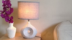 A bedside table with a lamp and a vase of flowers. - Mary's little house (San Juan Bautista)