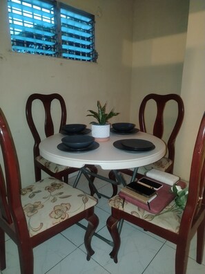 A dining table with four chairs, a potted plant, and a window with blue blinds.