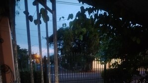 A gated entrance with a metal gate, a paved pathway, and a tree-lined background. - Mary's little house (San Juan Bautista)