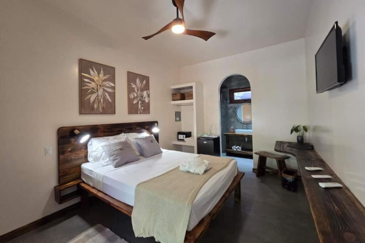 Un dormitorio con cama de madera, ventilador de techo, televisor de pared y obras de arte.