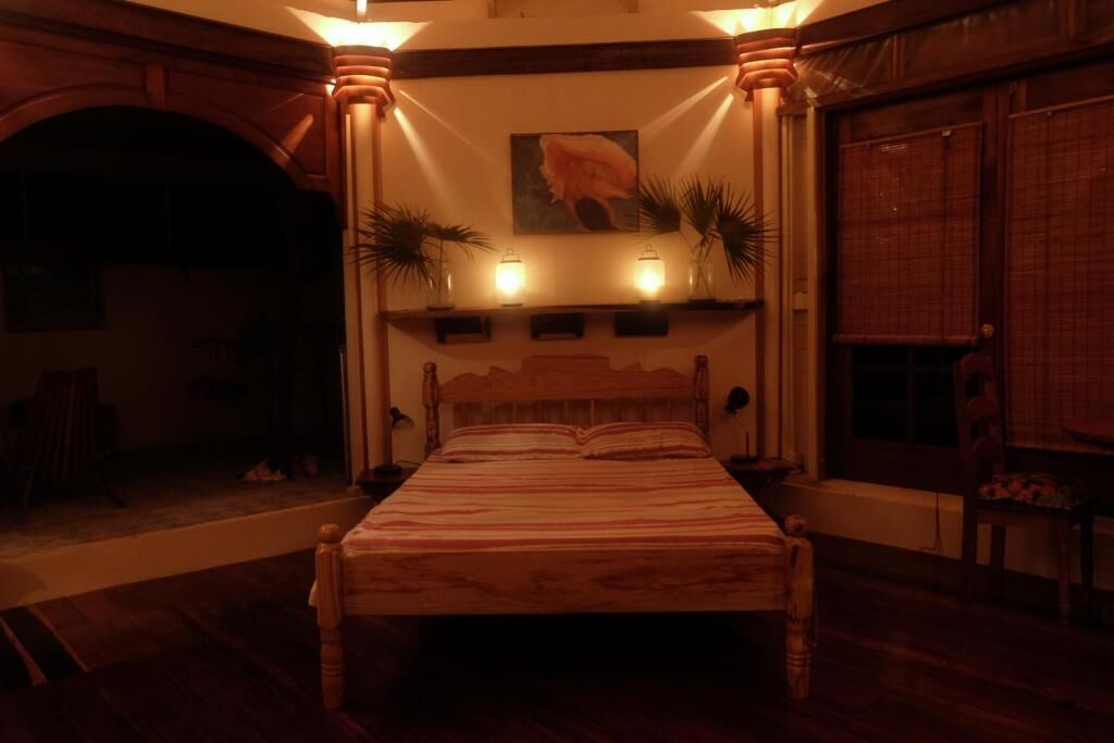 A bedroom with a wooden bed, a painting on the wall, and two potted plants.