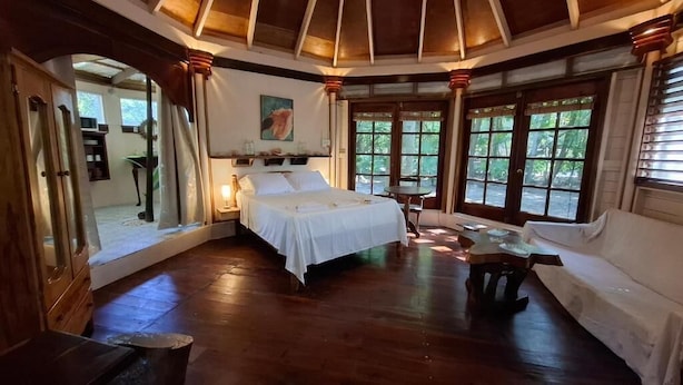 Ein Zimmer mit einem großen Bett, einem kleinen Tisch, einer Couch und einem Fenster mit Blick auf Grünflächen.