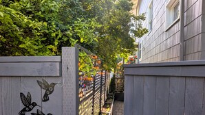 Un étroit sentier bordé de clôtures en bois ornées de découpes d’oiseaux, qui mène à un bâtiment doté d’une fenêtre.