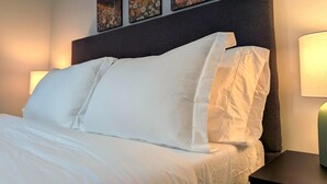 Un lit bien fait, avec du linge de lit blanc, une tête de lit sombre et trois tableaux encadrés accrochés au mur au-dessus.