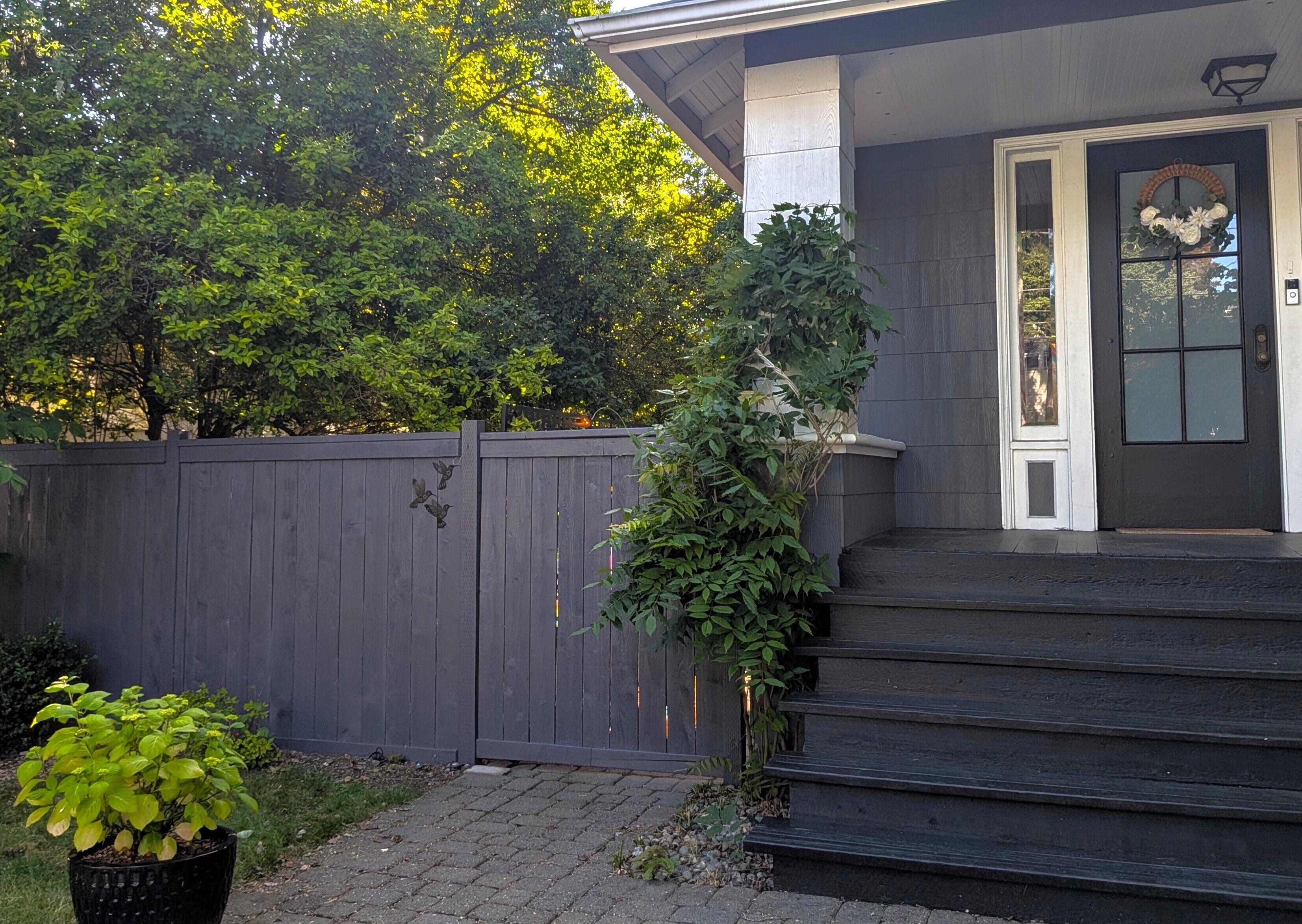 A residential house with a dark gray exterior, a front door with a decorative wreath, and a wooden fence.