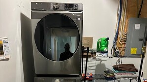 A laundry room with stacked washers and dryers, a utility cart, and a laundry basket. - Sleep & Grill | 5BR, Huge Yard, Smoker, BBQ (Fox Creek)