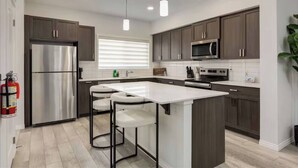 Una cocina moderna con armarios de madera oscura, electrodomésticos de acero inoxidable, una isla blanca e iluminación colgante.