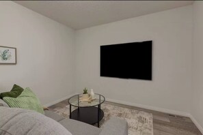 A living room with a flat-screen TV mounted on the wall, a round glass coffee table, and a grey sofa with green cushions. - Room-the Sunset Getaway SE (Calgary)