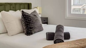 Una cama bien hecha con almohadas, una toalla enrollada y una colcha.