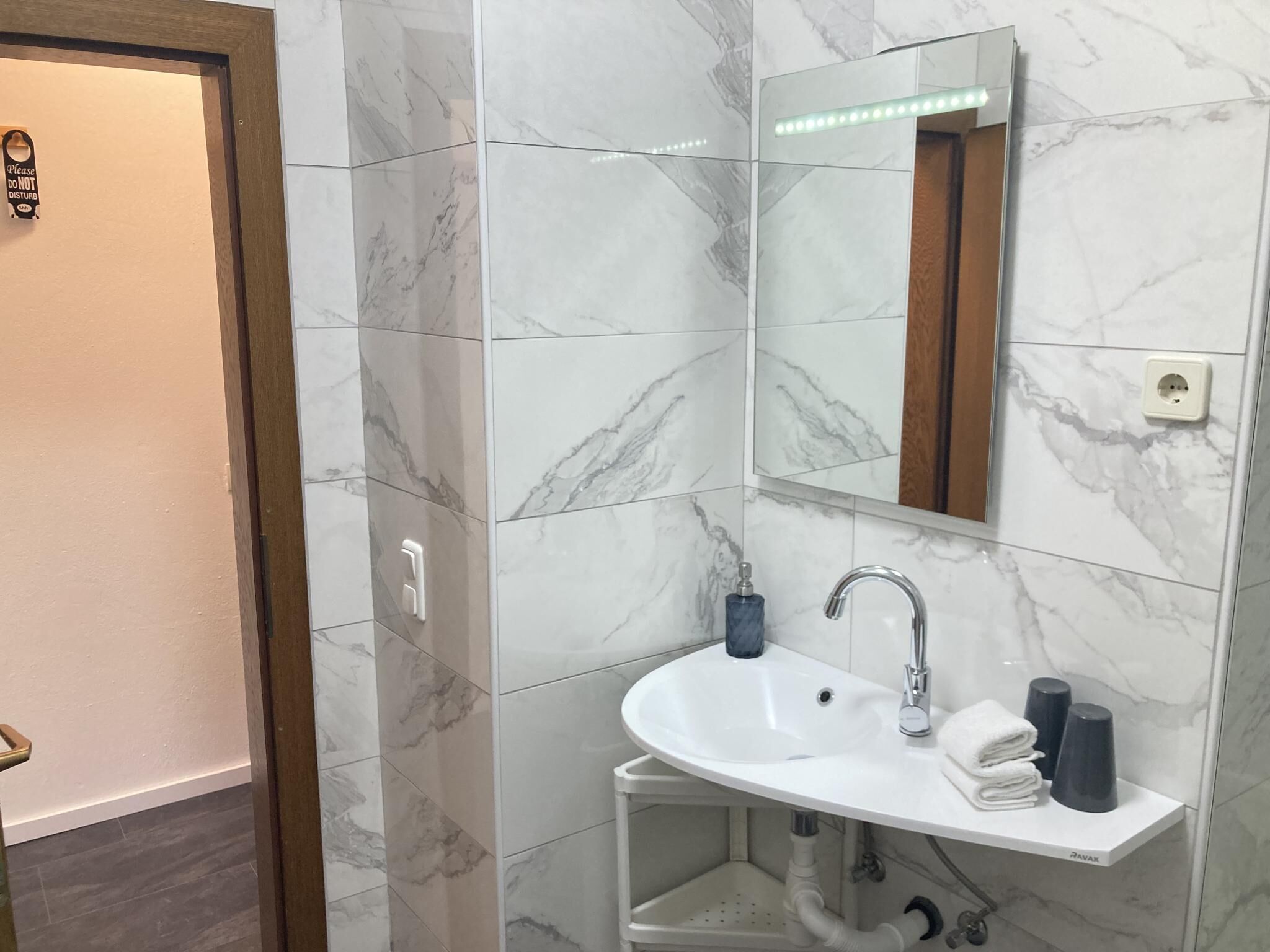 A bathroom with a white sink, mirror, and marble tiles.