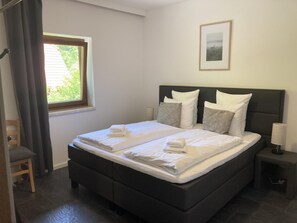 Ein Doppelbett mit weißer Bettwäsche, ein dunkles Kopfteil und ein Nachttisch mit Lampe.