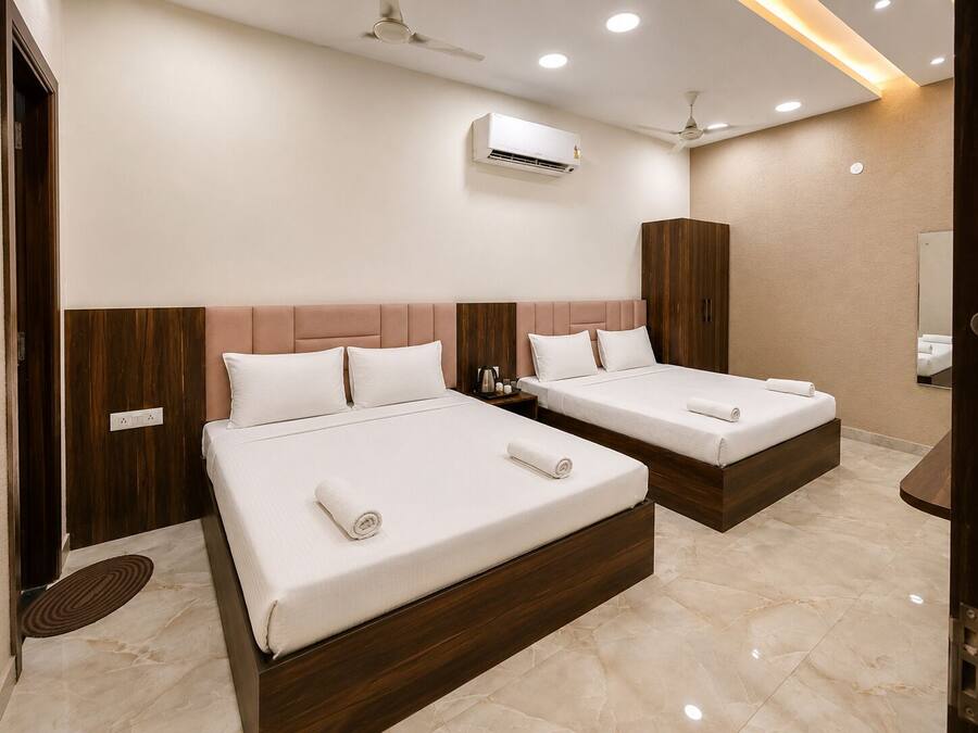 A hotel room with two beds, an air conditioning unit, a ceiling fan, and a bathroom with a mirror.