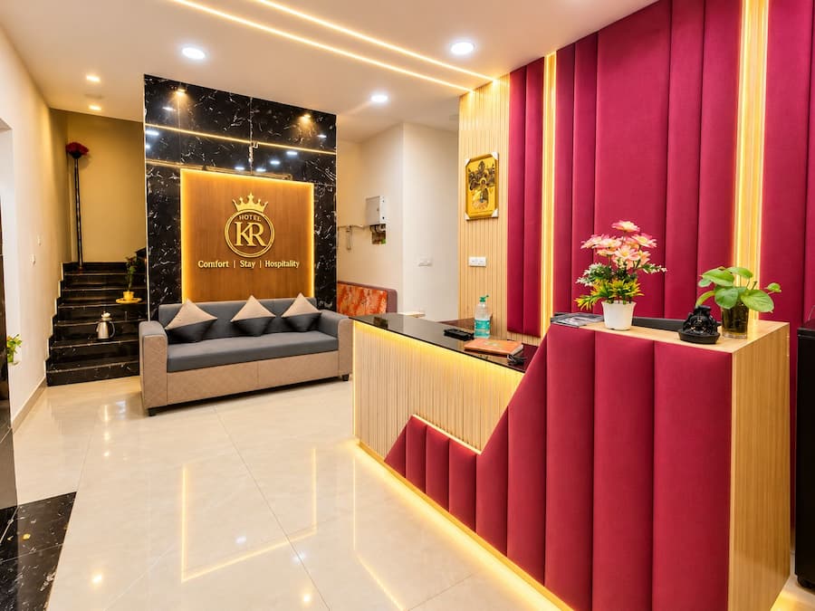 A hotel reception area with a marble wall, a sofa, a reception desk, and a staircase.