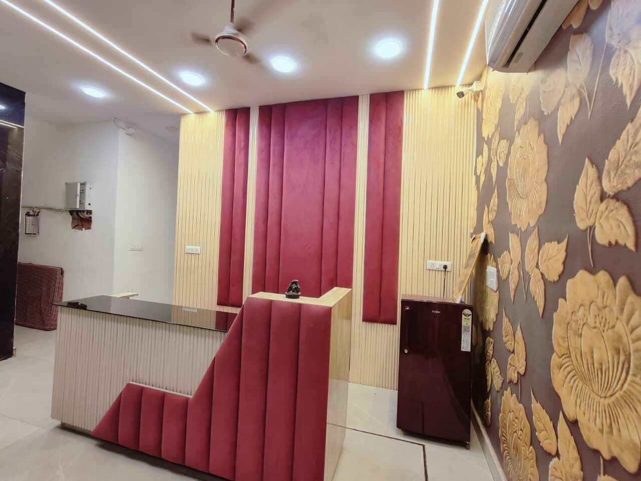 A reception desk with a red cushioned seating area, a small refrigerator, and a patterned wall.